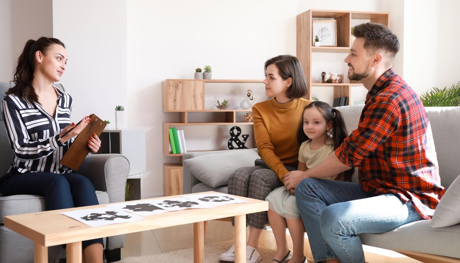 A diverse family sits on a couch in a warm living room, sharing smiles and discussing their feelings together.